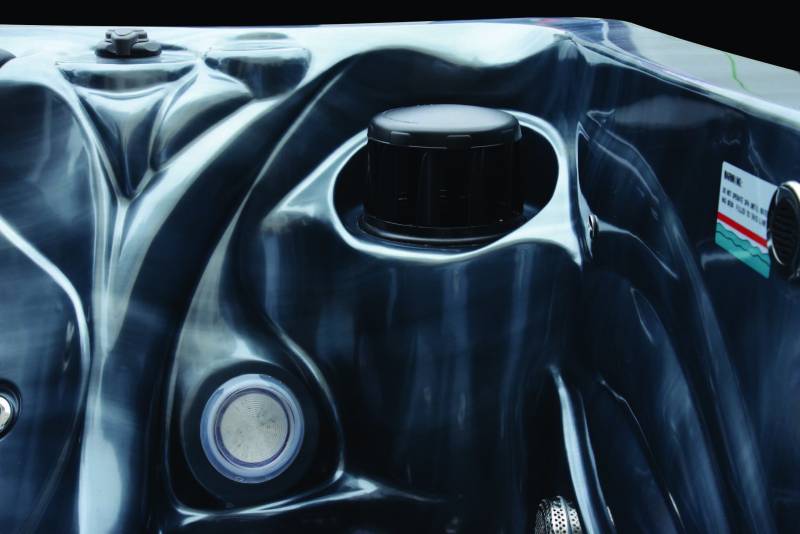 Intérieur de spa noir brillant avec formes ergonomiques. Un bouton de contrôle, un filtre noir et un jet visible. Autocollant d'avertissement.