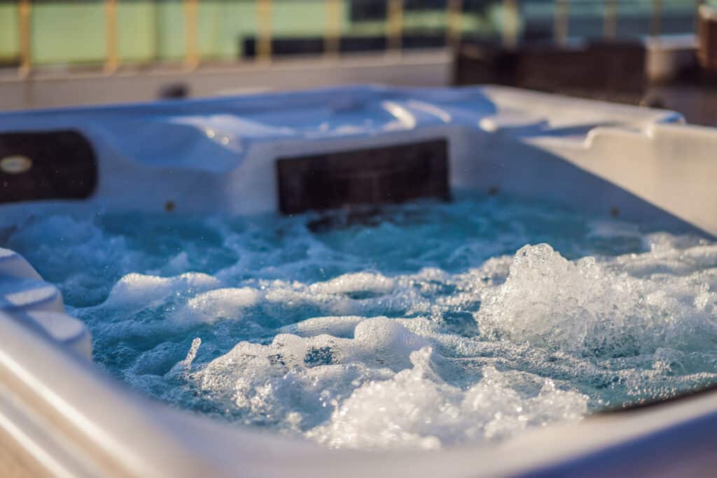 Jacuzzi d'extérieur blanc bouillonnant, rempli d'eau turquoise claire et de mousse. Bulles pétillantes sous le soleil sur une terrasse.