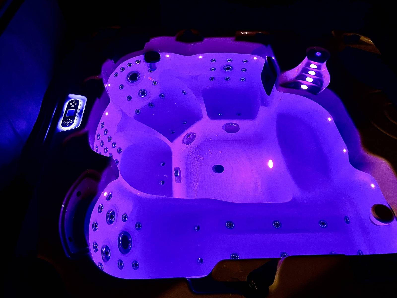 Jacuzzi moderne avec éclairage LED violet, de nombreux jets de massage, et un panneau de commande numérique. Ambiance relaxante.
