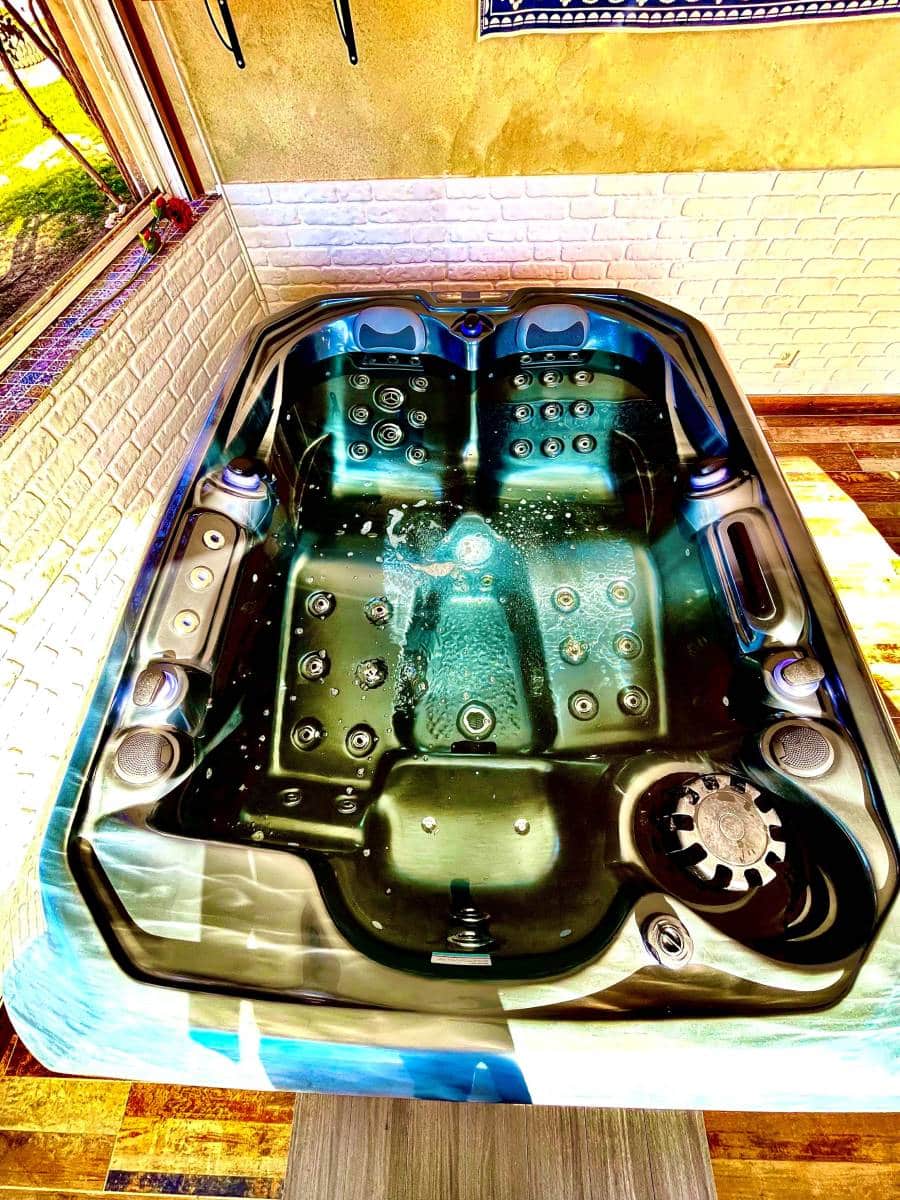 Jacuzzi moderne avec eau bouillonnante et jets actifs, intérieur bleu-vert, entouré de murs texturés et d'une fenêtre lumineuse.