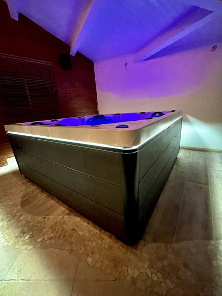 Jacuzzi moderne avec éclairage LED violet dans une salle de détente intérieure, mur en bois et sol carrelé texturé.