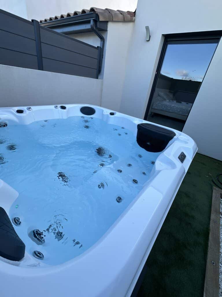 Spa jacuzzi extérieur moderne sur terrasse privée. Spa jacuzzi moderne blanc sur une terrasse privée. L'eau bleue bouillonne à côté d'une baie vitrée reflétant le ciel et montrant une chambre intérieure.